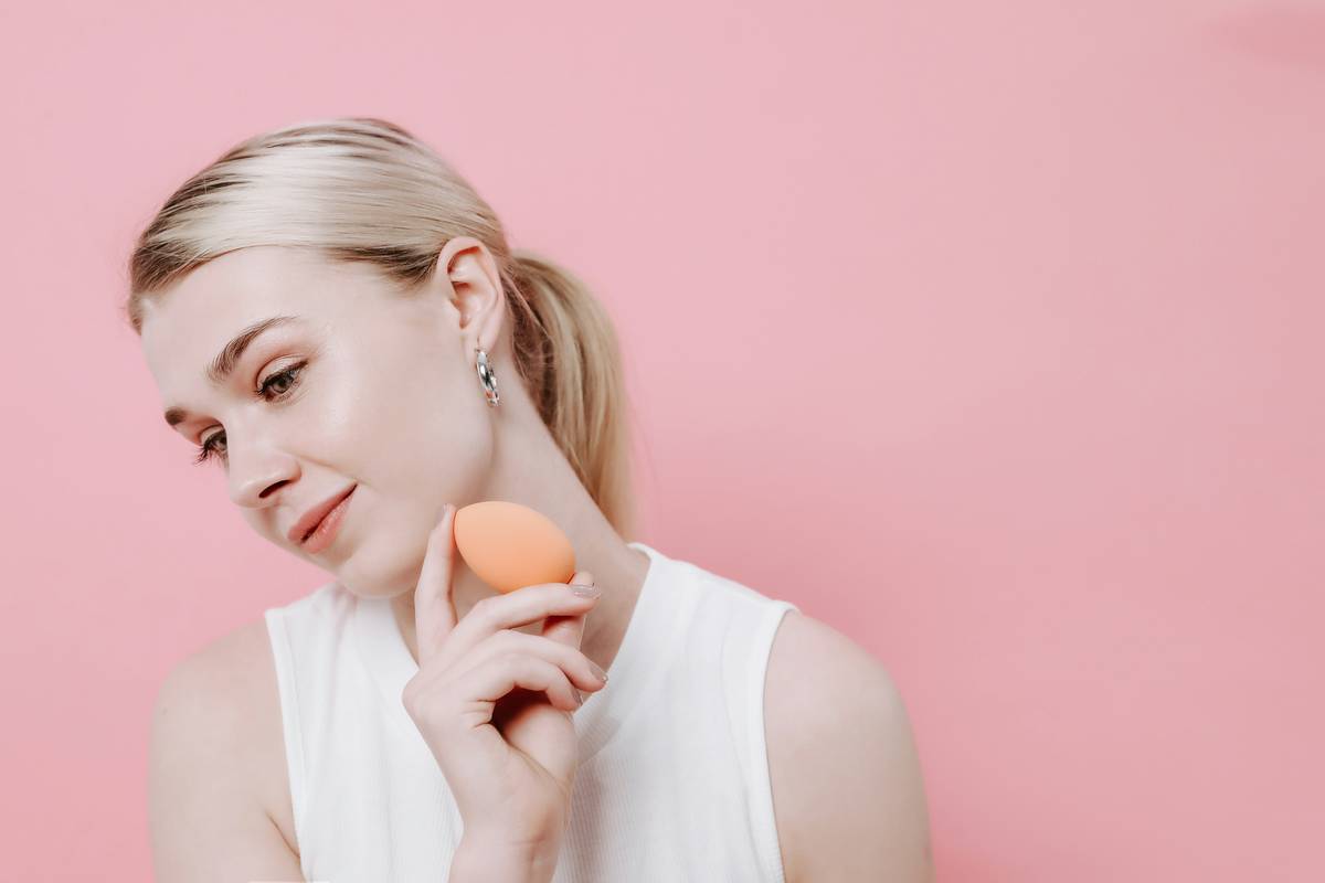 Woman using a damp blending sponge makeup tool to apply liquid foundation evenly across her cheekbone